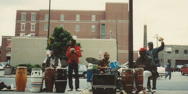 Street musicians playing drums and percussion instruments in an urban setting.