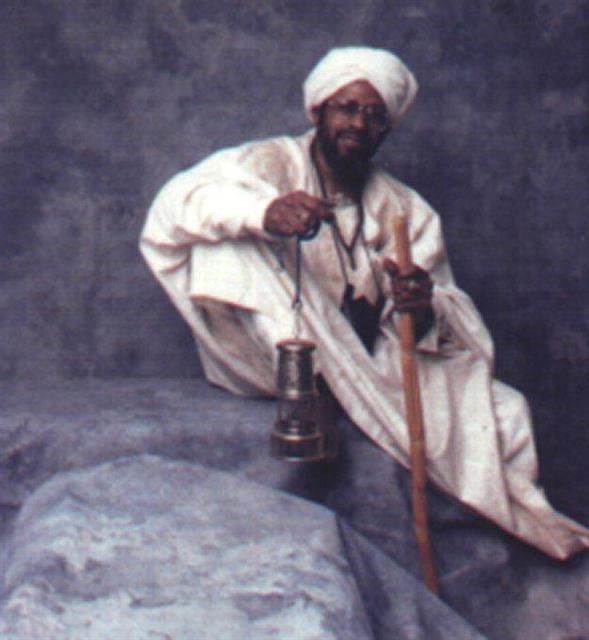 Man in traditional attire holding a lantern and staff.