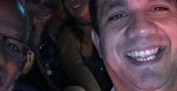 A close-up selfie of four people smiling in a dimly lit setting.