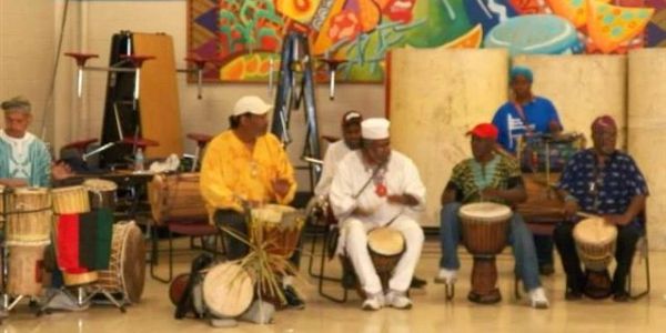 A group of six men playing traditional African drums indoors.