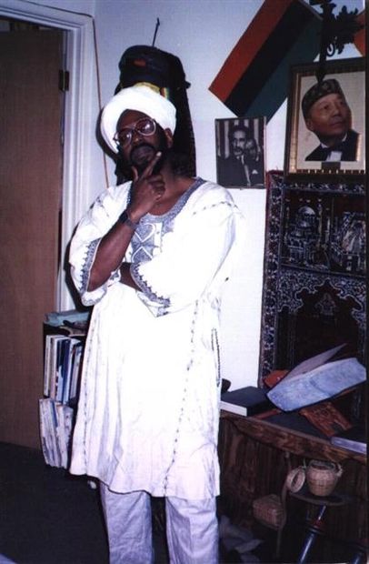 Man in traditional white attire and turban posing thoughtfully indoors.